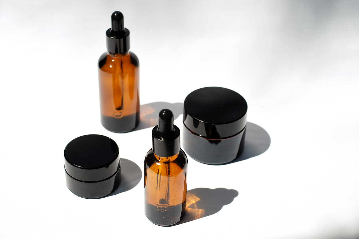 Serum Bottles and Black Cosmetic Containers on White Background